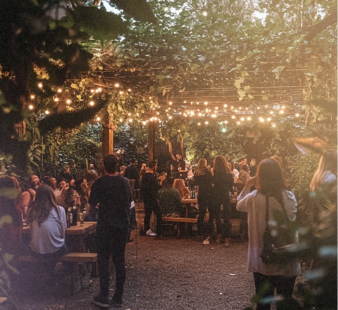 Ambiance conviviale lors d'une soirée en extérieur sous des guirlandes lumineuses, avec des tables et des participants socialisant.