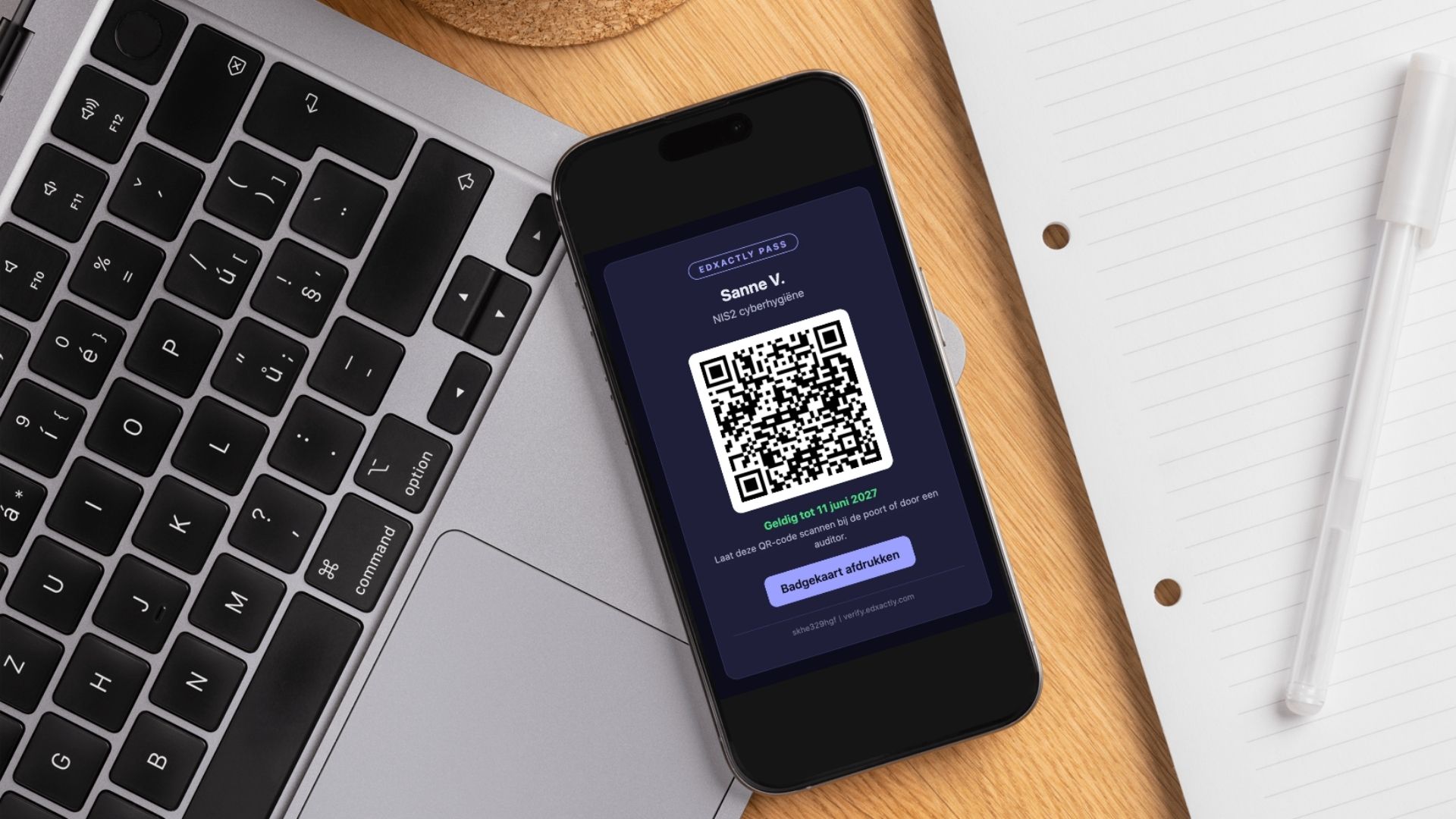 Laptop and iphone on a desk next to a notebook and a pen, iphone shows an example of an EdXactly Pass and QR code