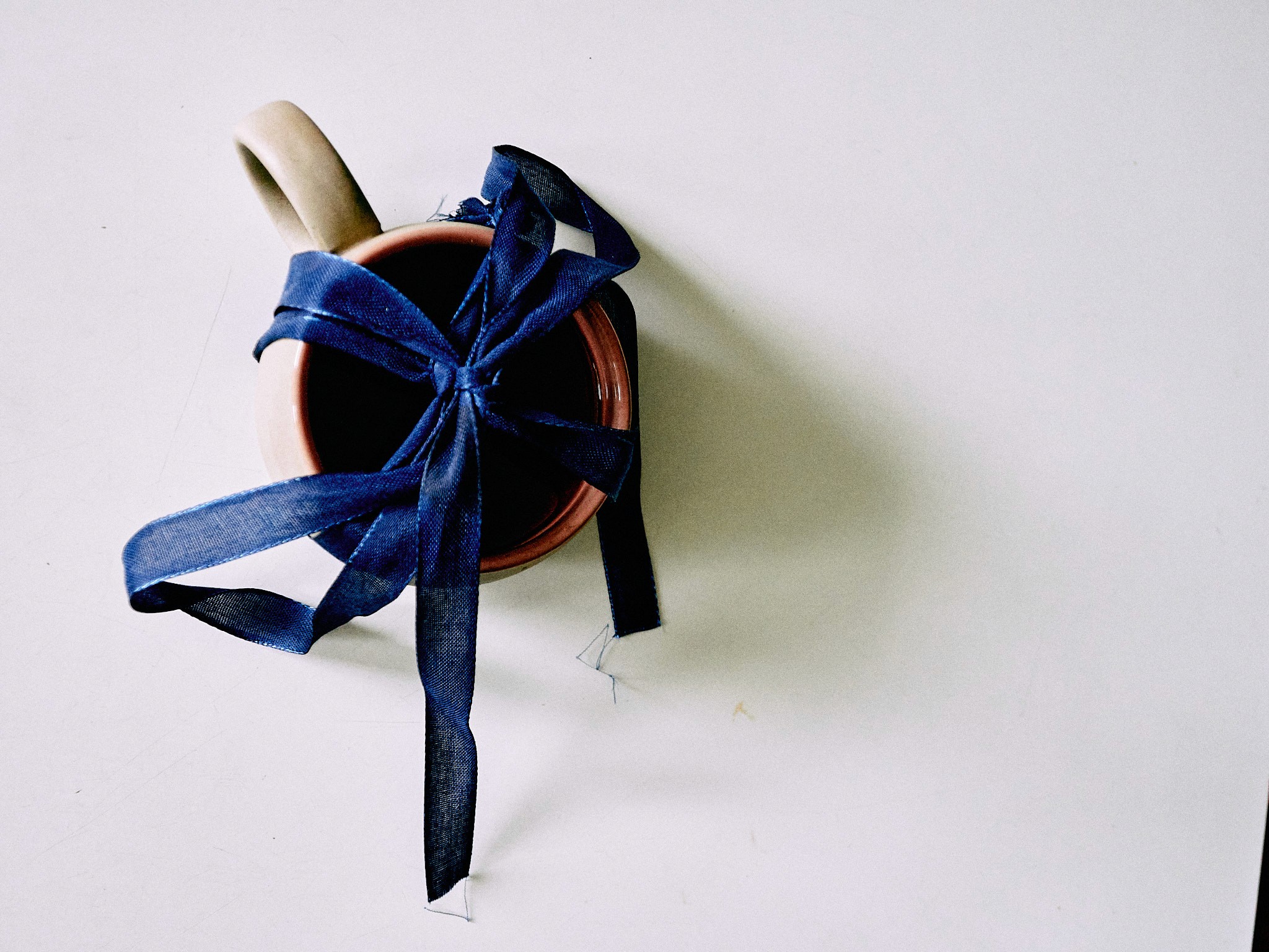 Beige Tasse mit blauem Geschenkband, seitliche Nahaufnahme – kreative Stillleben-Fotografie von Ovid Dernbach.