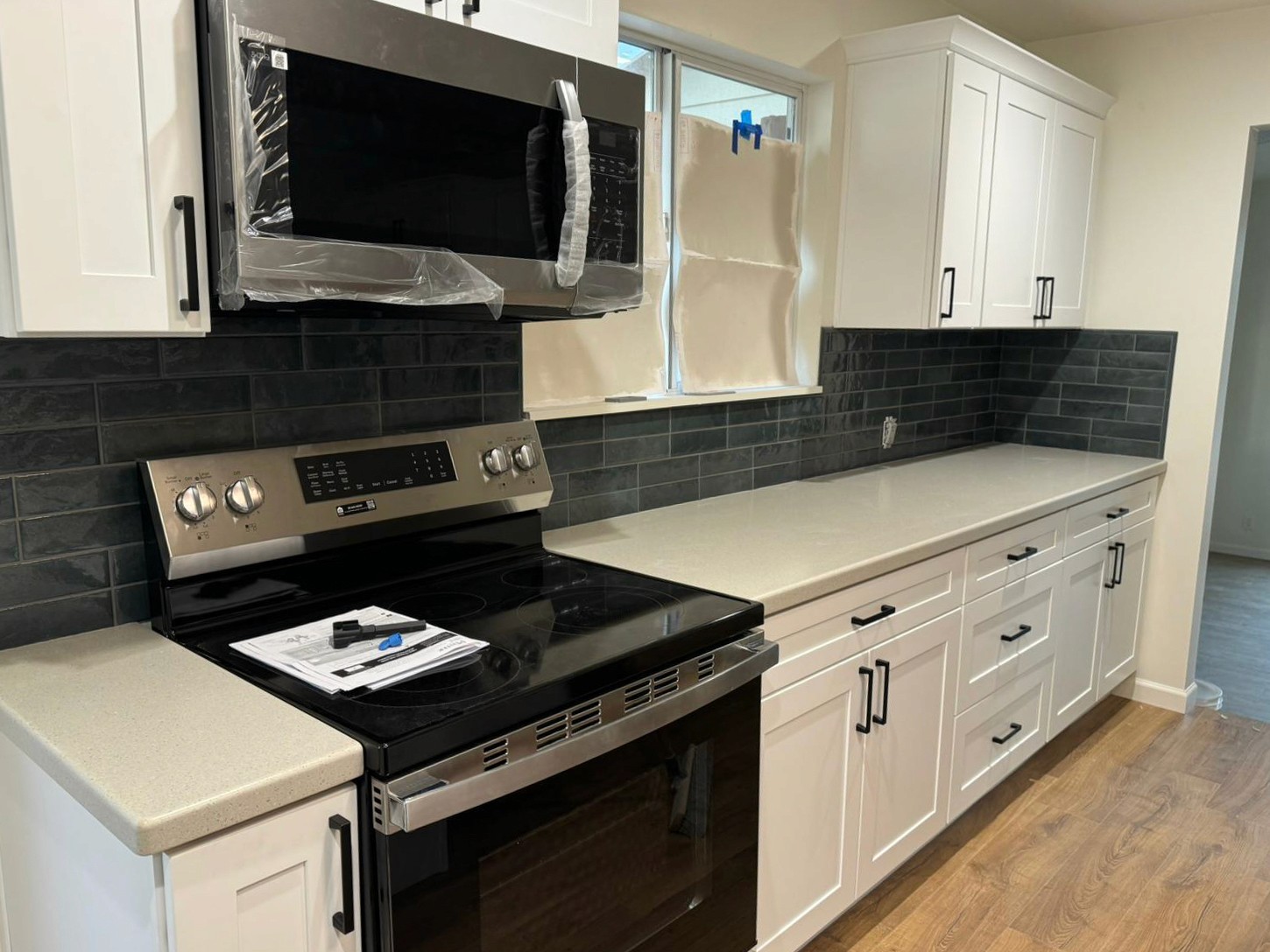 Contemporary kitchen with a white countertop, black subway tile backsplash, and a stainless steel microwave and oven, complemented by white cabinets.