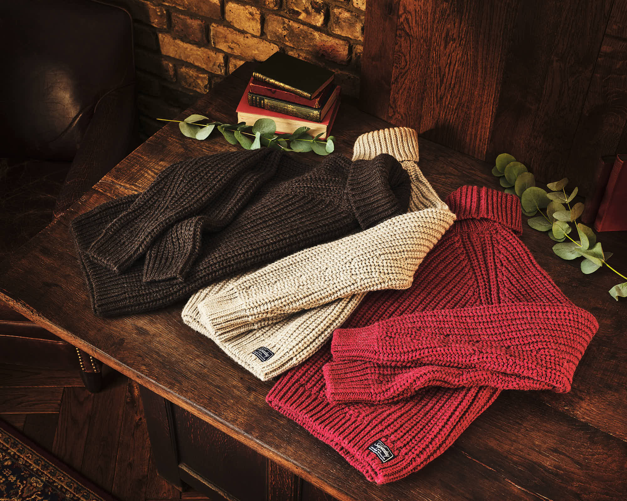 Cozy knitted sweaters in dark brown, cream, and red on a rustic wooden table.