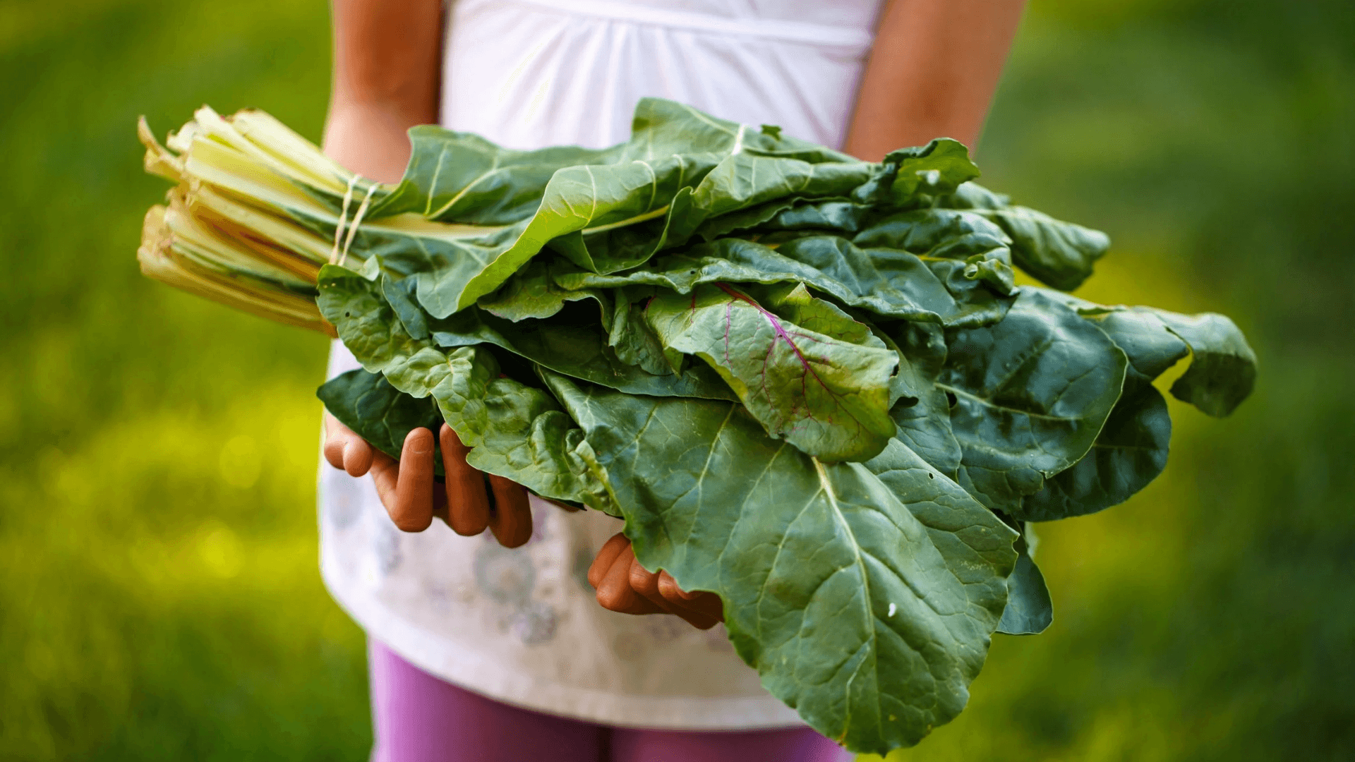 Child holding a bundle of freshly harvested leafy greens outdoors