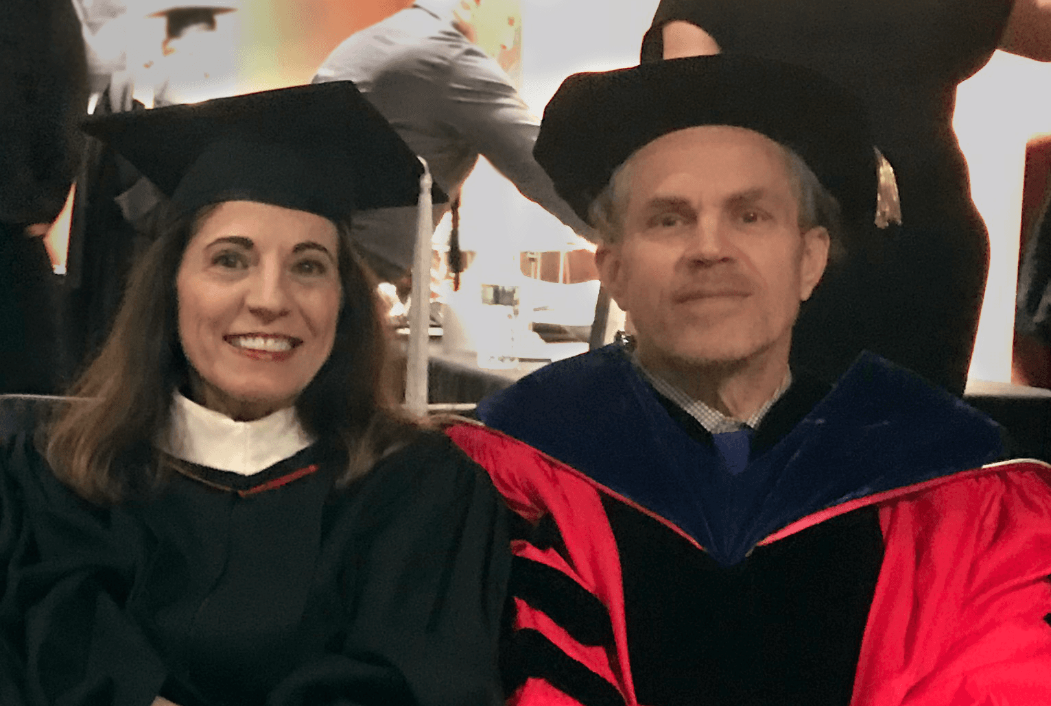 A photo of two people wearing black and red robes for the graduation ceremony.