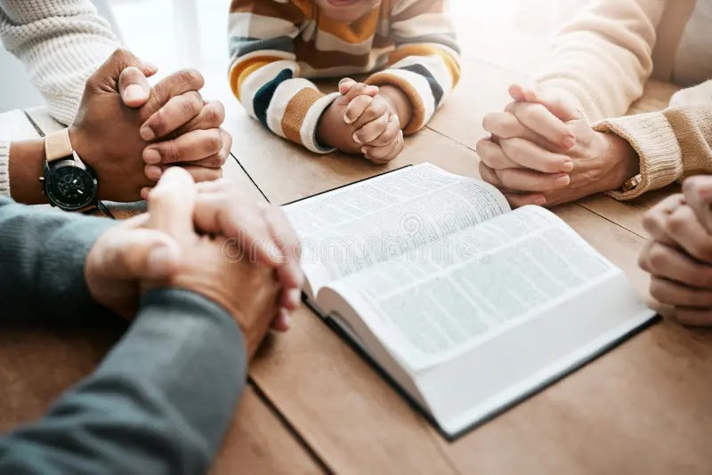 Conversion Truth for Families - Family's hands clasped together in prayer next to a Bible