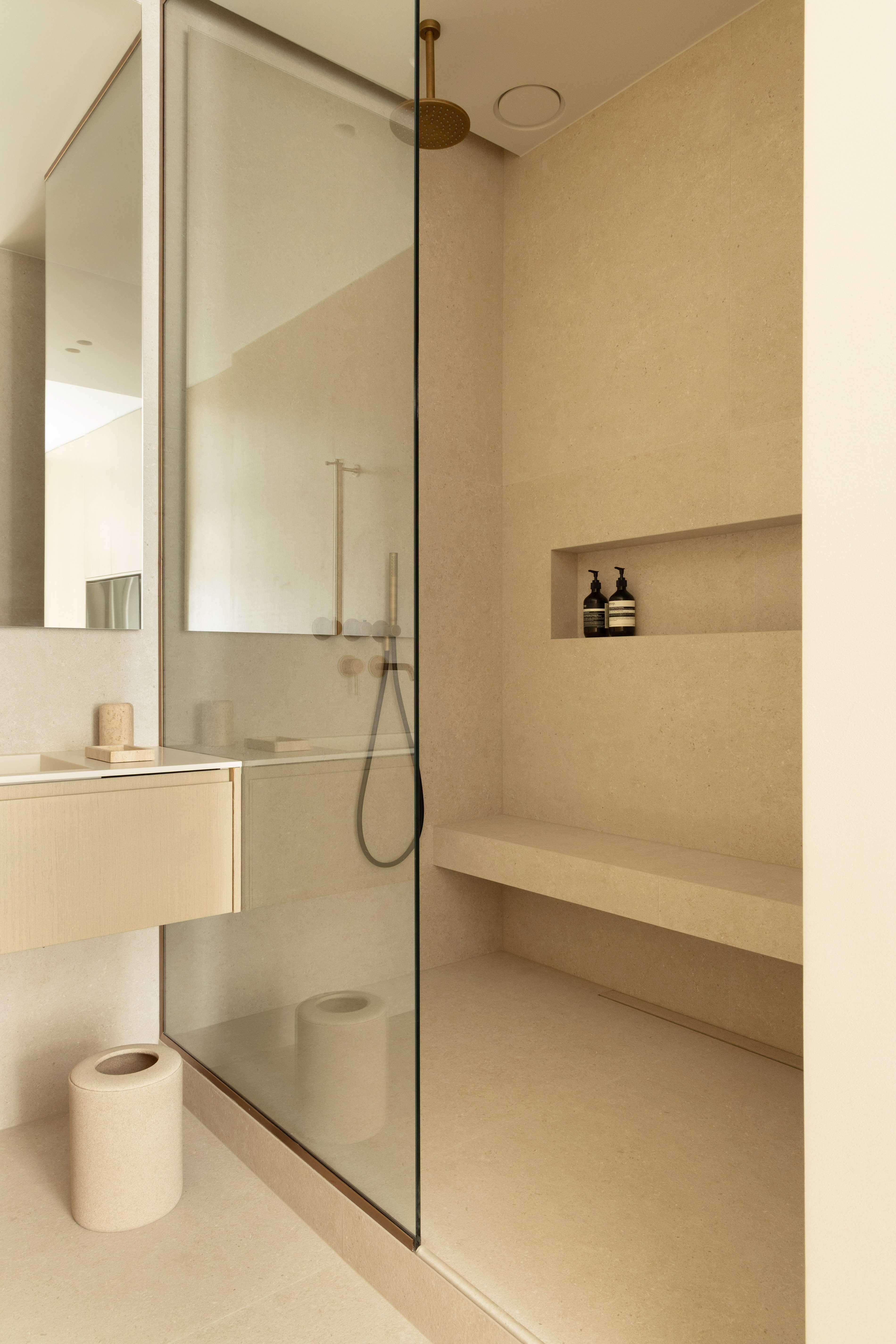 Douche italienne avec pommeau de plafond dore, banc en pierre, niche avec produits et paroi vitree