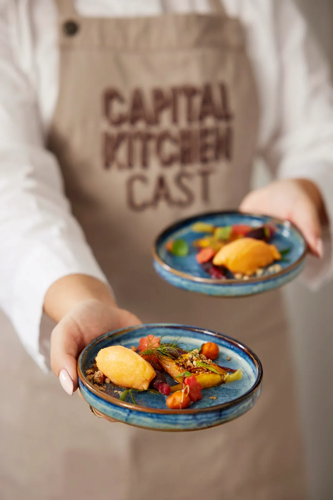 A person in an apron holds two plates of food, serving them to someone off-frame.