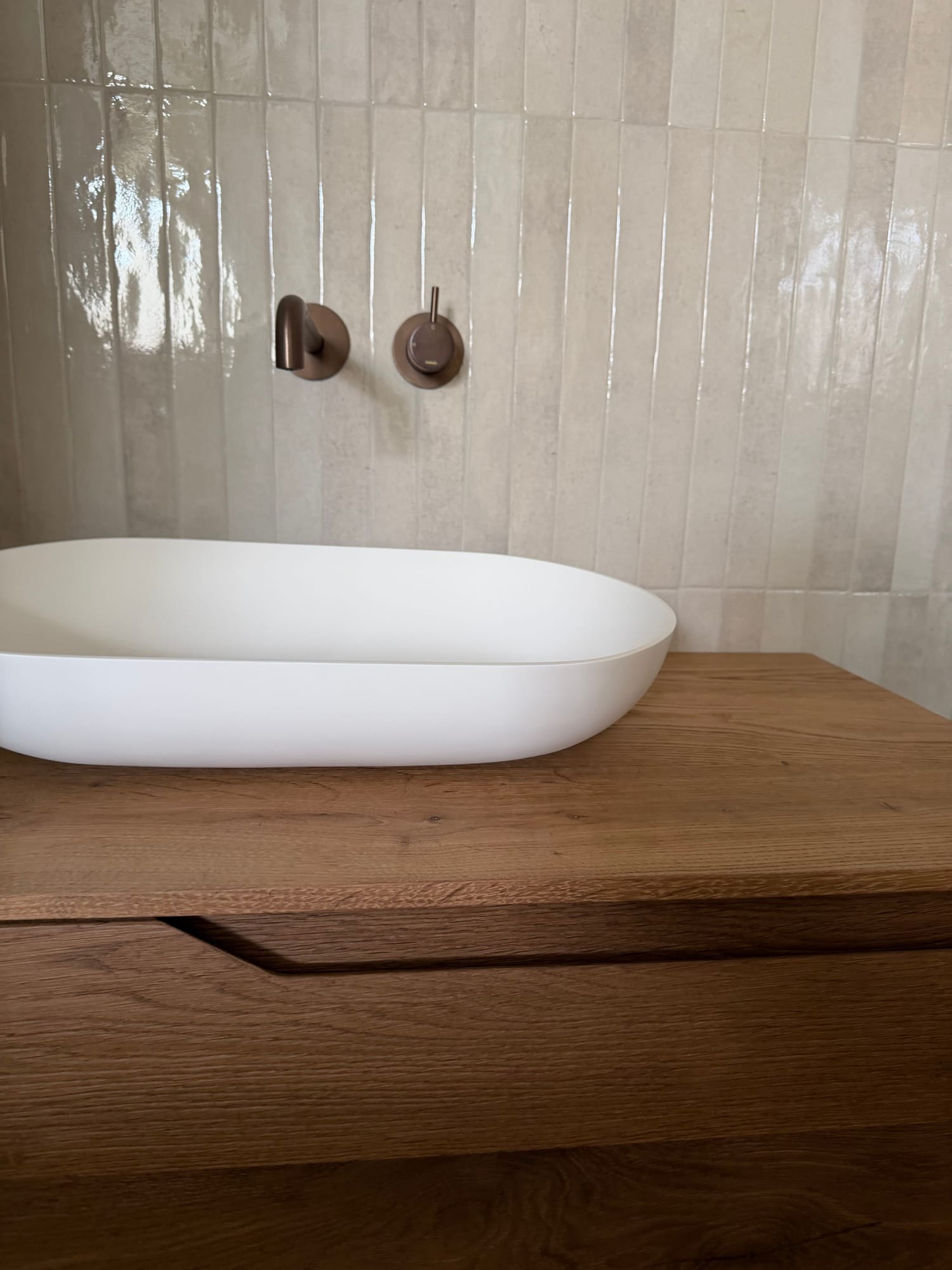 White basin on a wooden vanity with copper-toned taps