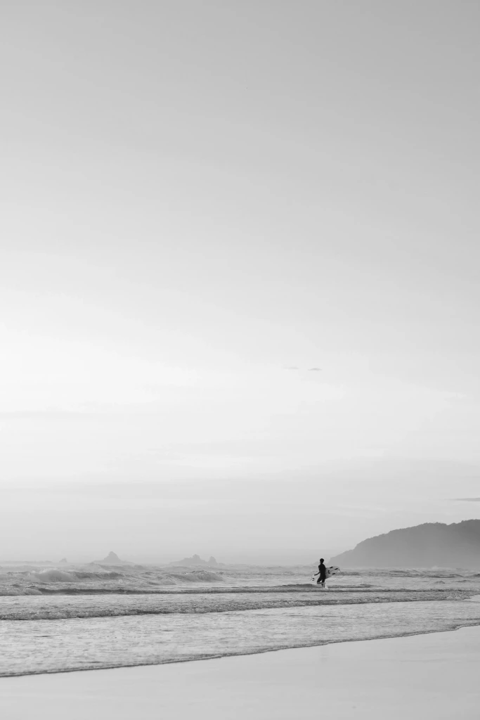 Surfer walking into the ocean at Byron Bay, New South Wales, a popular coastal destination for travellers arriving by private jet charter