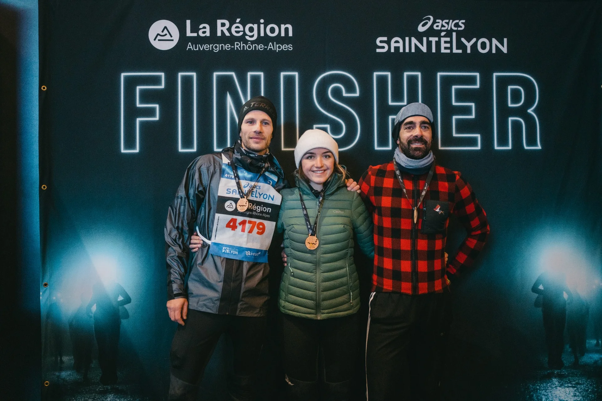 Portrait des finishers de la SaintéLyon portant leur médaille, photographiés par Outdoor Perspectives devant le panneau d’arrivée