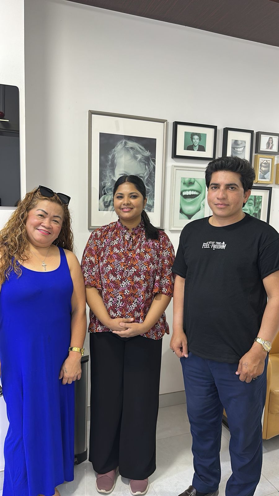 Three people standing in the reception area with framed dental photographs