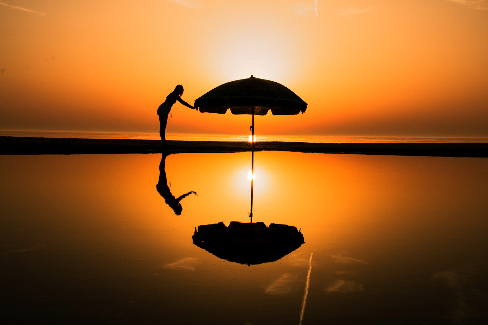 Silhouet van een parasol bij zonsondergang, waarbij de dramatische kleuren van de lucht en de schaduw van de parasol een sfeervol beeld creëren