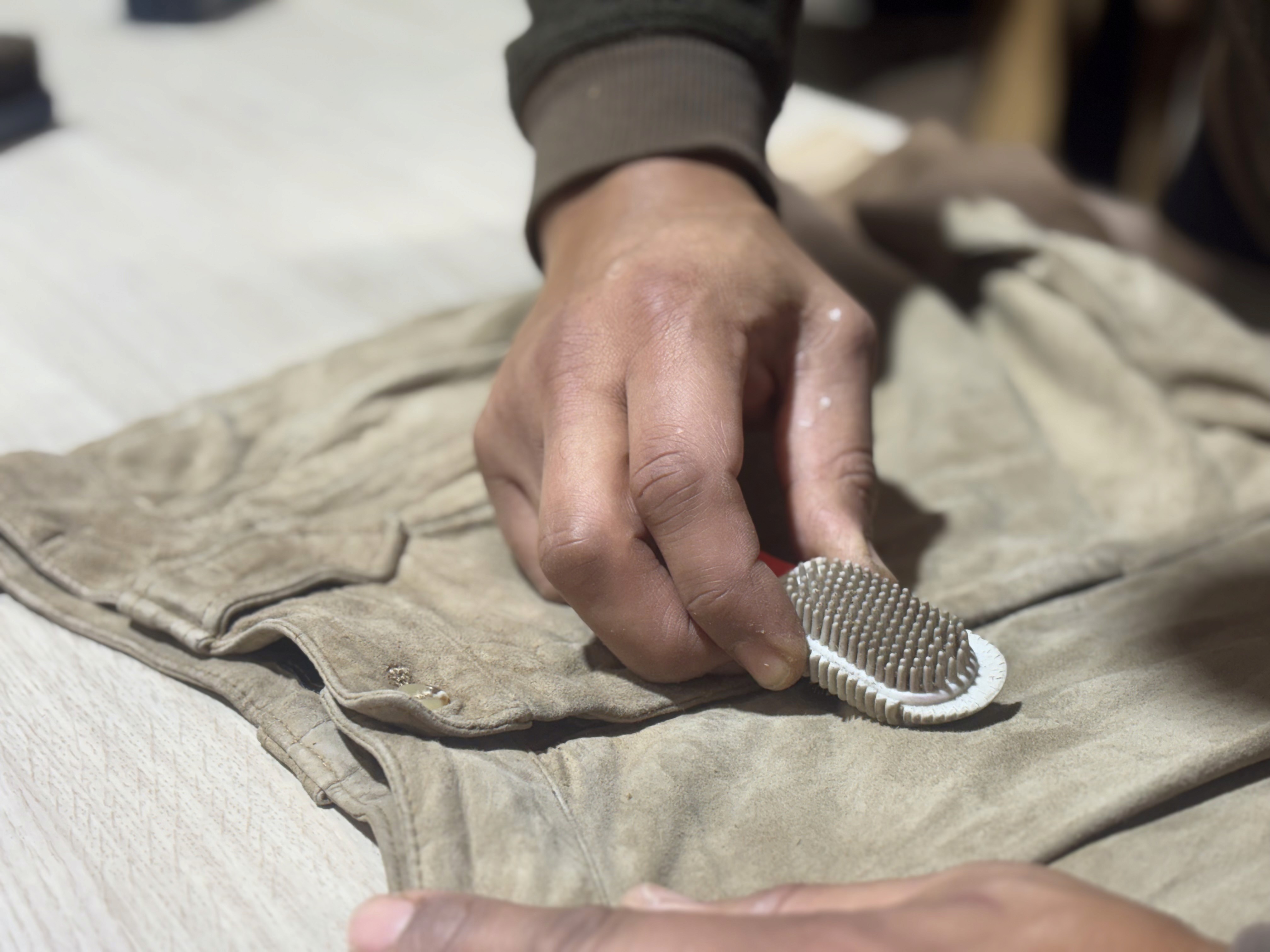 Person brushing a suede garment with a brush to clean and restore the nap.