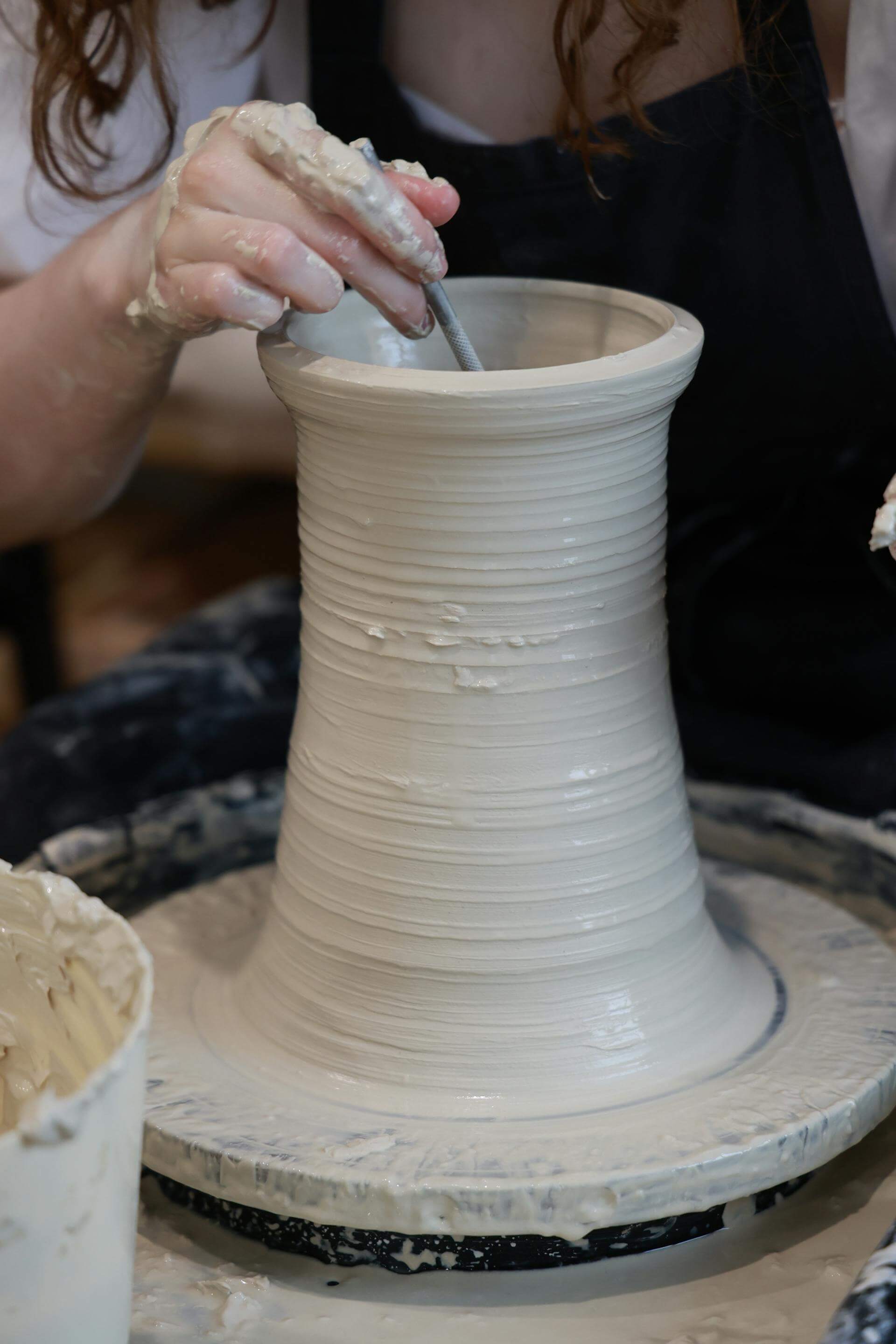 A woman skillfully shapes clay on a potter's wheel, creating a beautiful pot with her hands