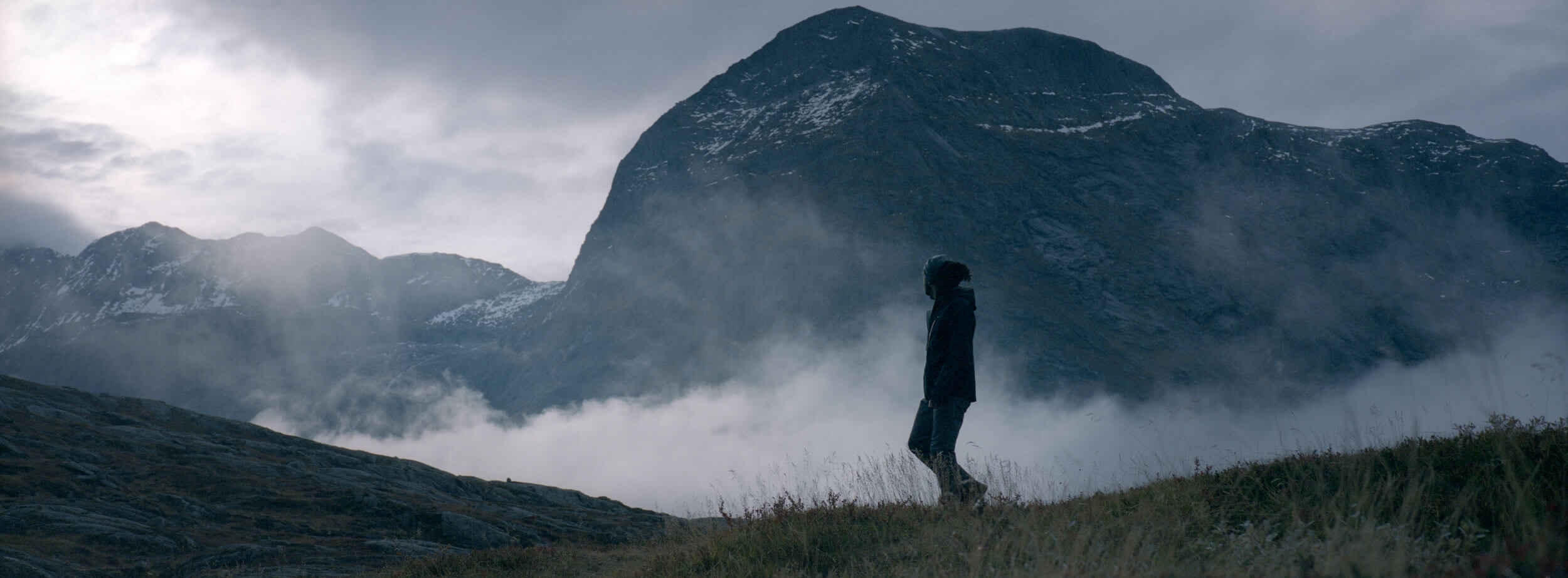 A person walking hrough the mountains in front of other mountain peaks in the background at the end of the day shot on a Hasselblad XPan 