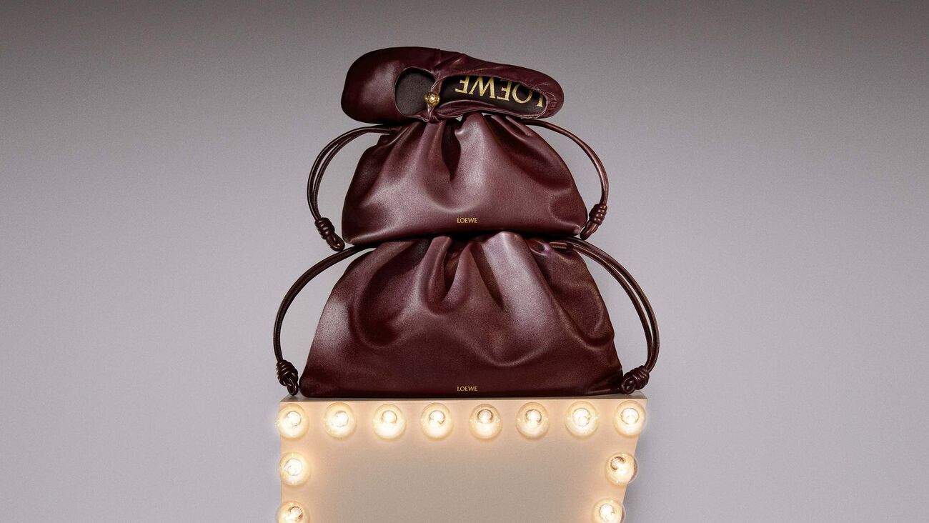 Focused young man in a mint green jacket staring ahead, with a fencing sword vertically aligned with his face, rooftops of a European city in the background.