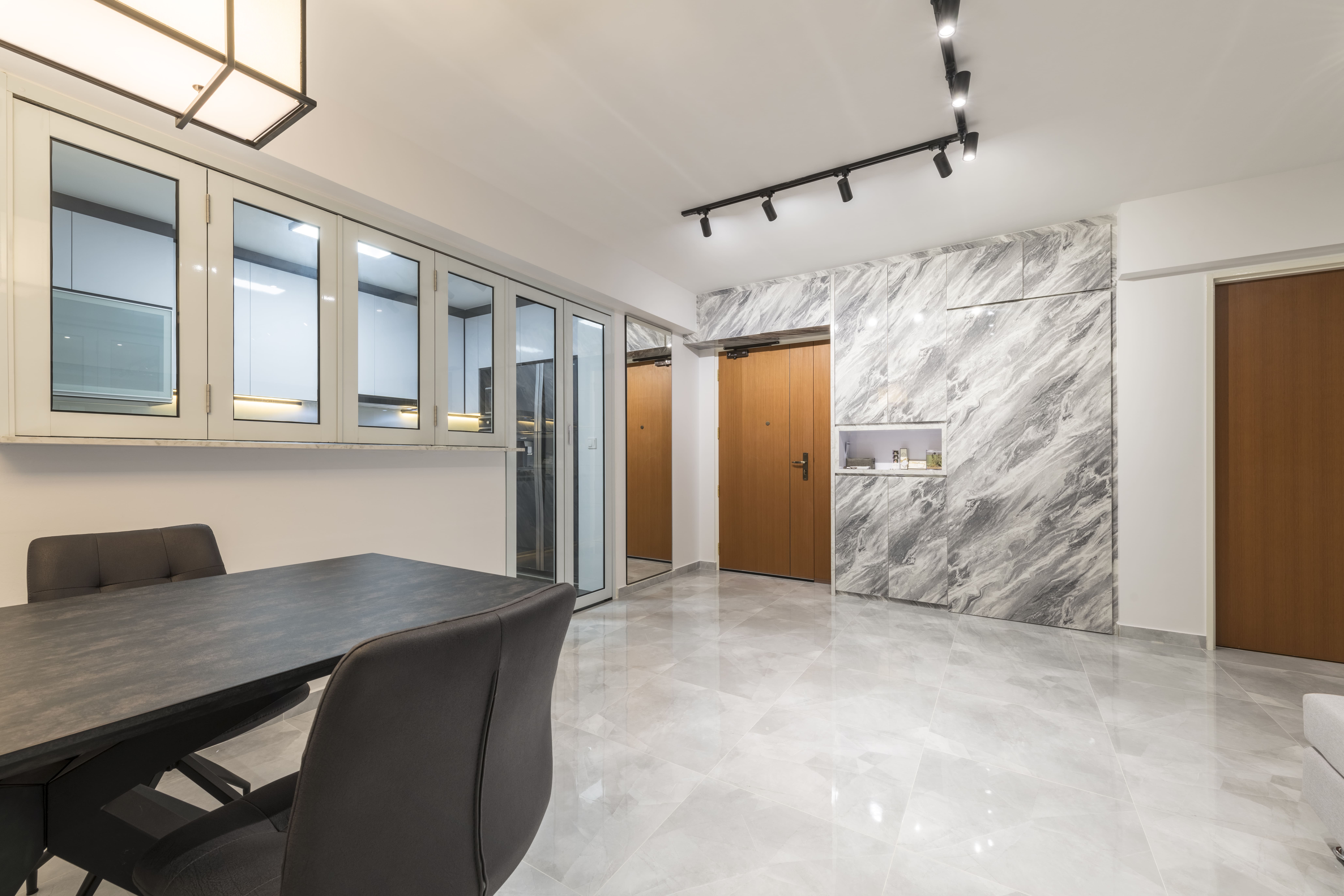 A striking marble-textured feature wall with concealed storage enhances the entryway, complemented by mirrored cabinetry that reflects light and expands the space visually.
