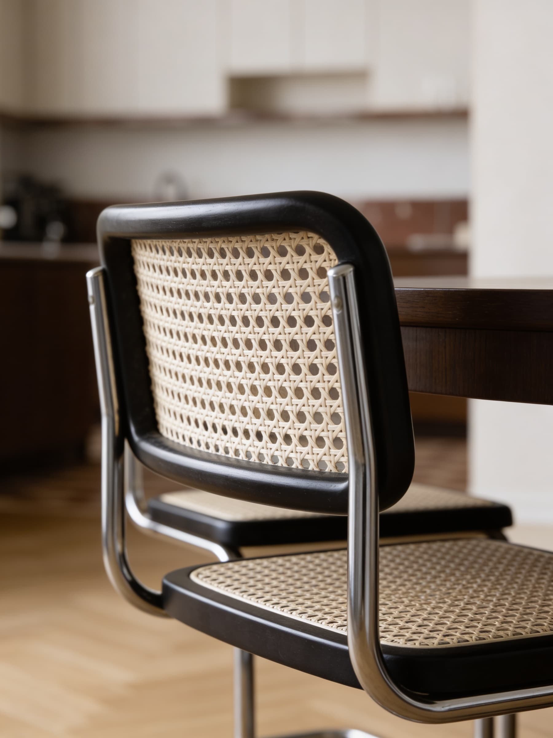 A modern dining room features a sleek, black-framed chair with woven cane backing and seat, positioned next to a wooden table, creating a minimalist and elegant interior design aesthetic.