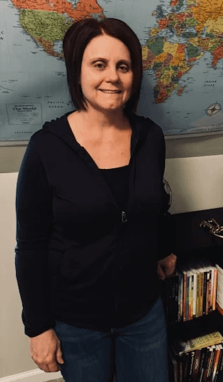 A young person with long, wavy hair sits in front of a plain background, looking directly at the camera.