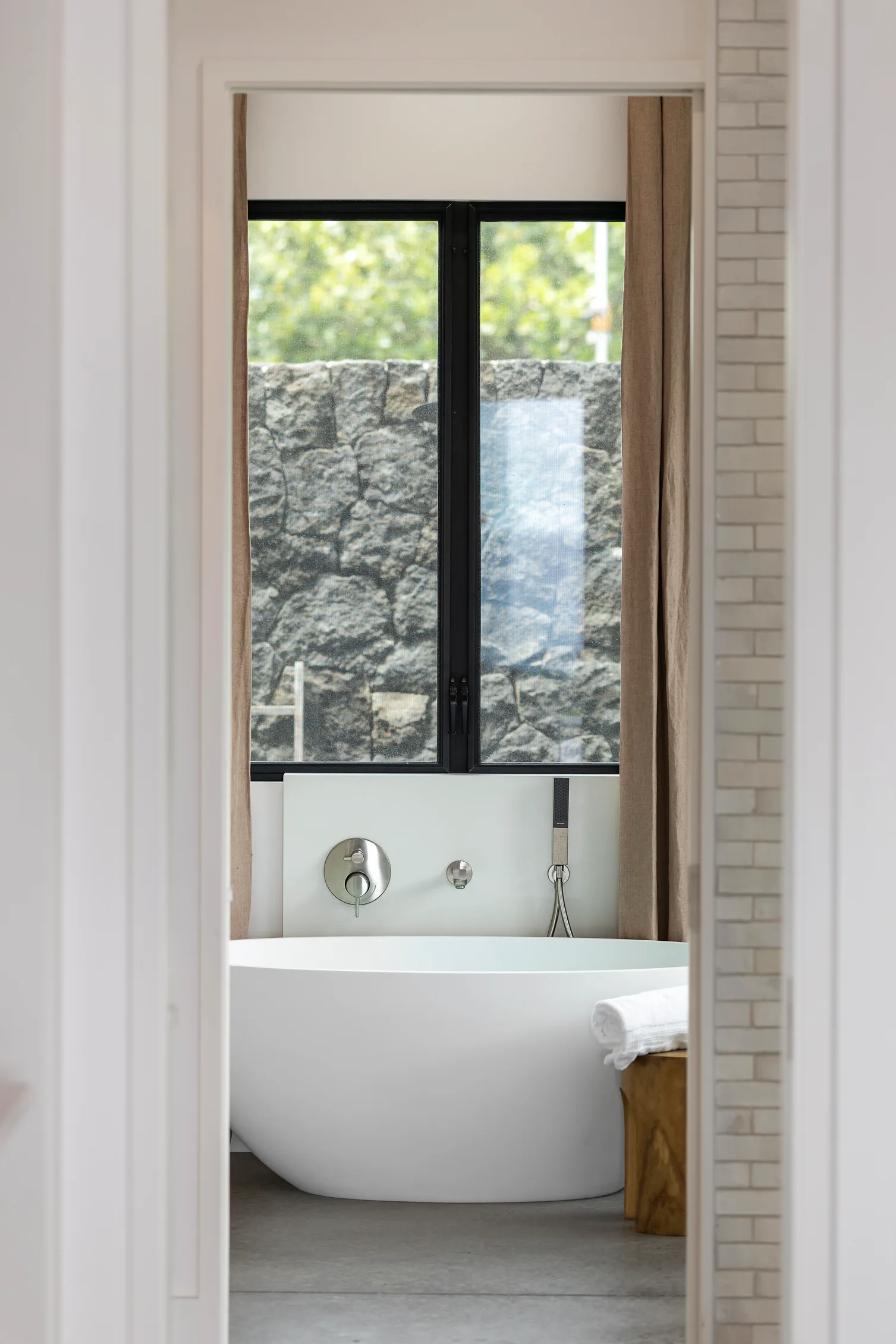 bathtub next to window with Hawaiian lava rock wall in background.
