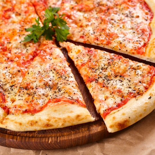 Pepperoni pizza with a garnish of parsley on top, displayed on a wooden board. A slice is slightly pulled away.