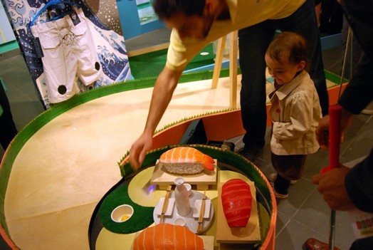 a dad and his kid are playing with a ball on a mini-golf course