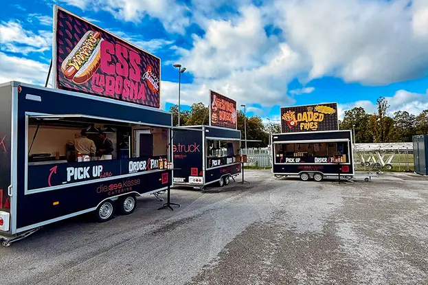 A food truck illuminated from within, showcasing a variety of food and drink items against a dark backdrop.
