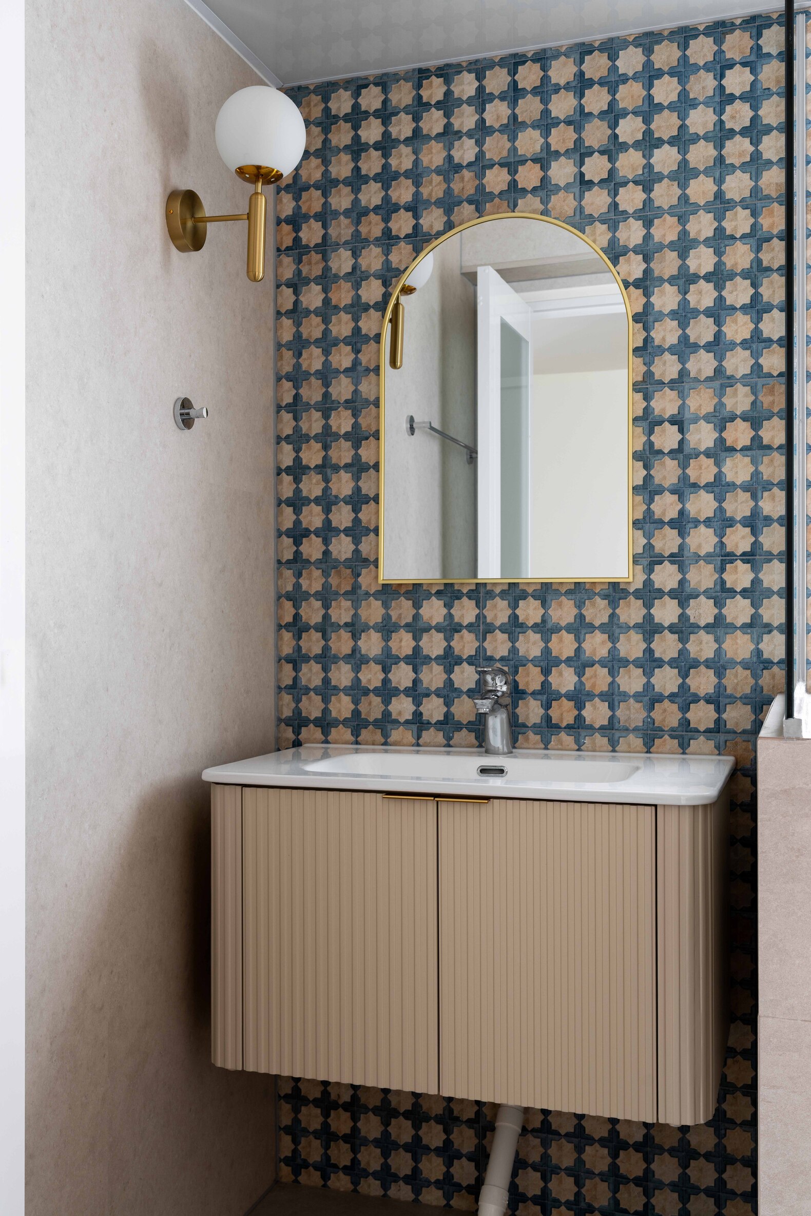 Modern bathroom vanity with patterned tiles, round mirror, and brass wall sconce lighting.