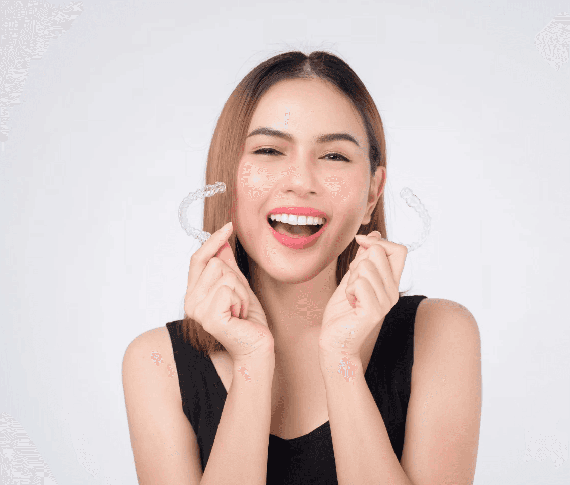 Invisalign in Dubai with a woman smiling confidently, holding her clear aligners, highlighting discreet and effective treatment.