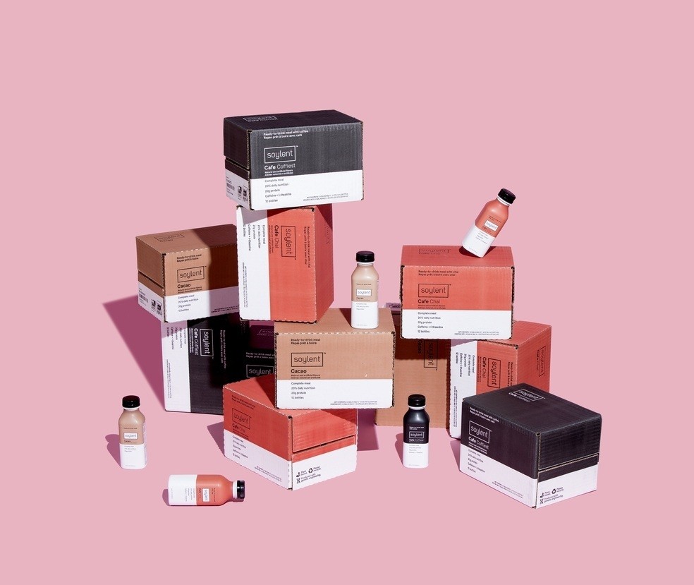 A stack of Soylent bottles and packaging on a pink background