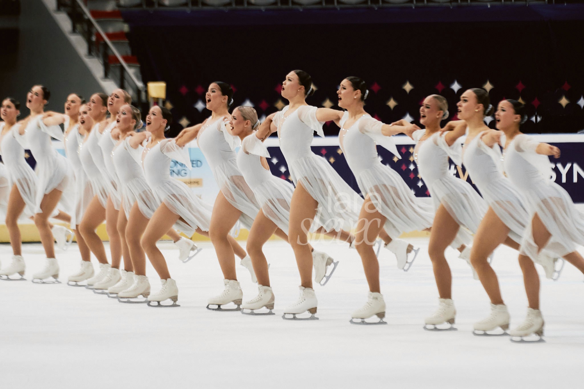 16 Synchroneiskunstäuferinnen in einer Reihe auf dem Eis. Team Unique. ISU Synchronized Skating Championships 2026 in Salzburg. Fotografiert von Lara Slevec.