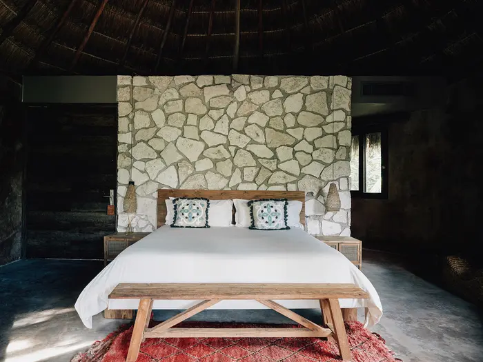 Arena Room en Nômade Tulum resaltando la espaciosa cama con almohadas, tapete y una impresionante arquitectura.