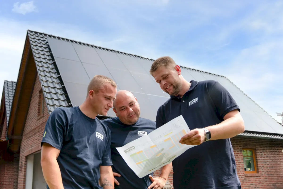 Drei Männer besprechen Baupläne vor einem Haus mit Solaranlage