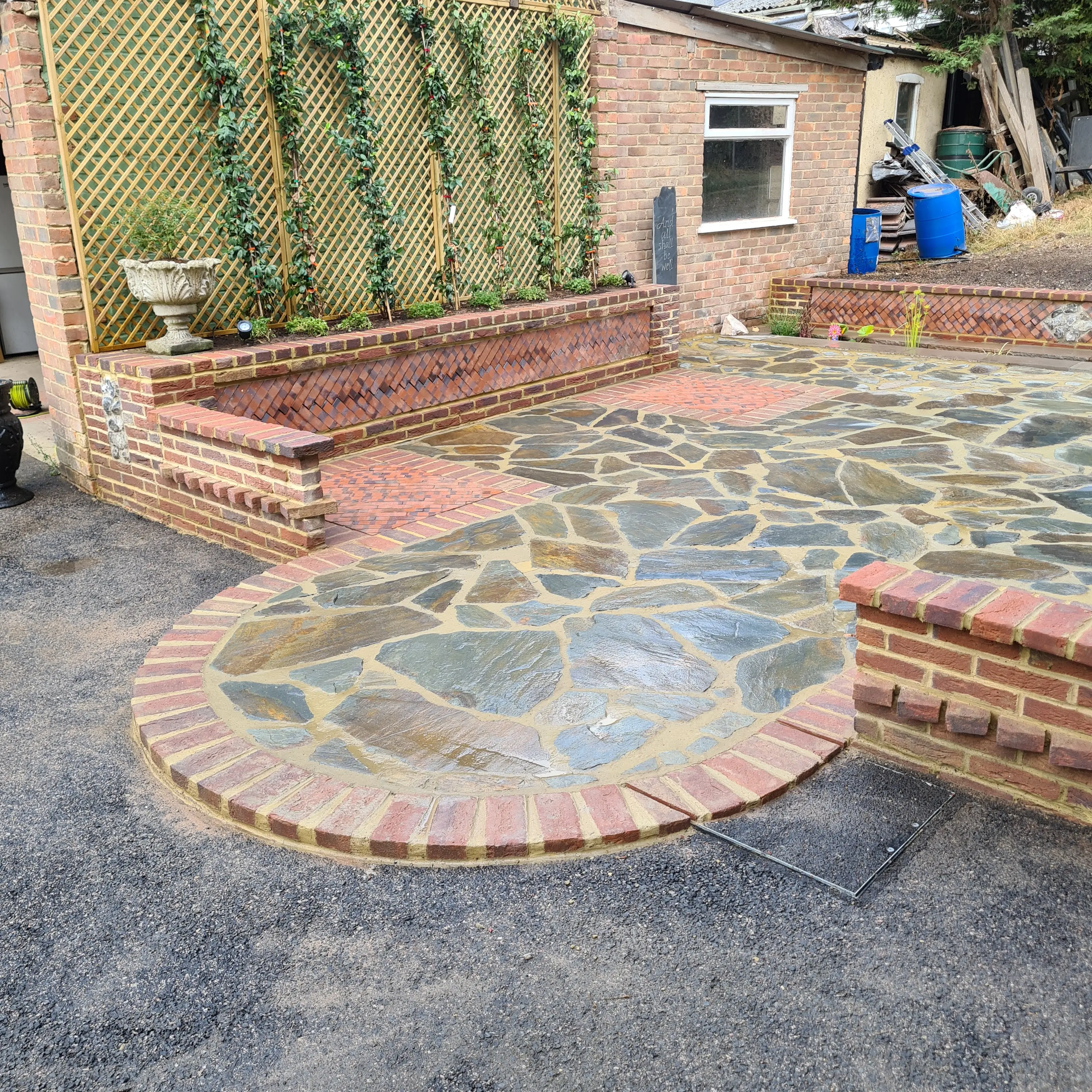 A circular stone patio with a decorative water feature surrounded by greenery and a person in the background.