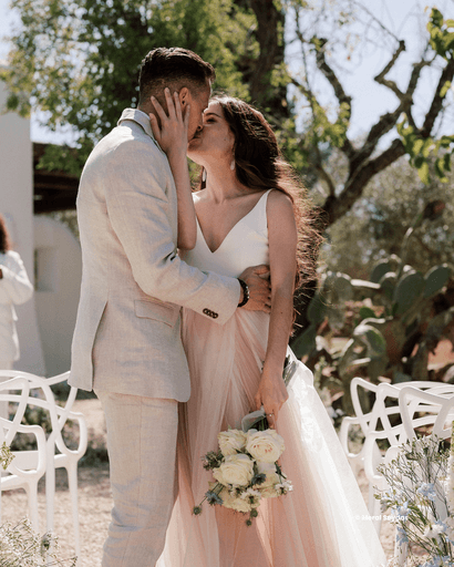 Een bruid en bruidegom delen een romantische kus tijdens hun huwelijksceremonie in de buitenlucht — een intieme en stijlvolle destination wedding vol trouwinspiratie.