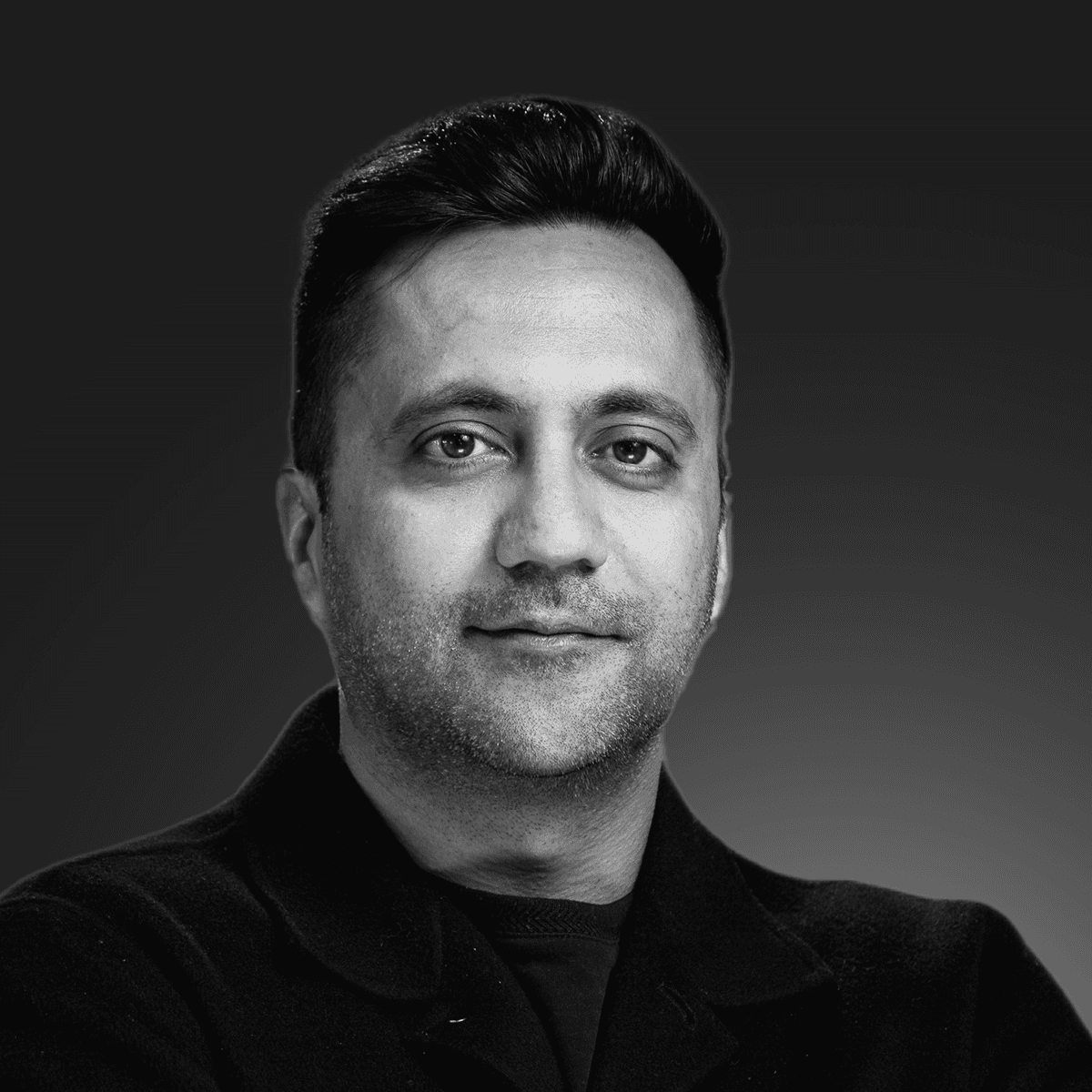 A confident person with short, styled hair and a leather jacket poses against a dark backdrop.