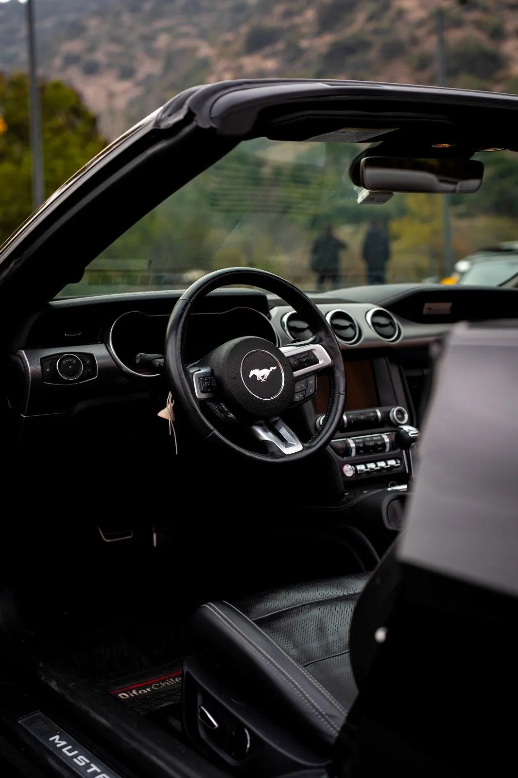 Interior del Ford Mustang convertible con volante, tablero y asientos negros vistos desde la puerta