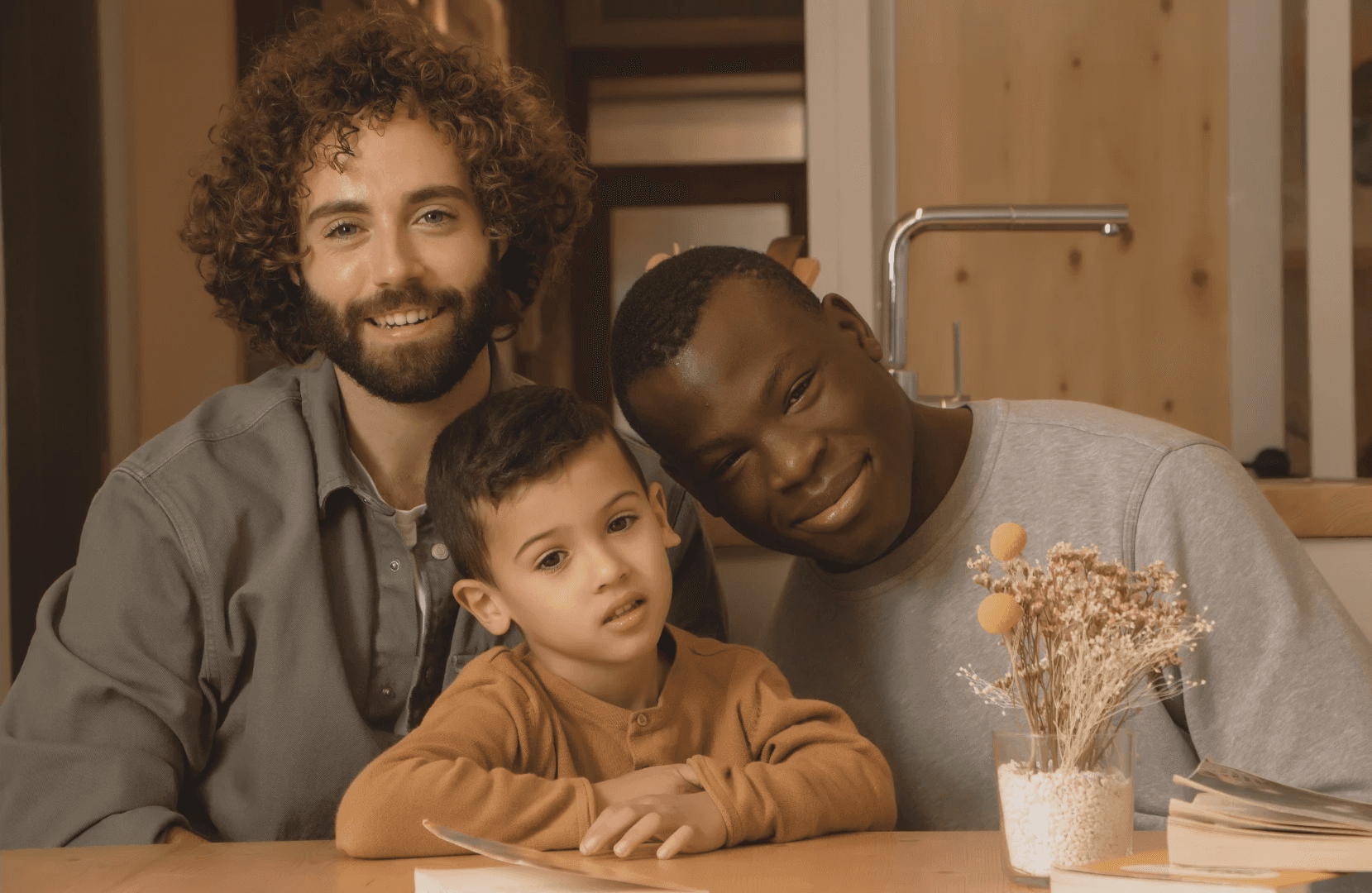 A cheerful family portrait featuring two adults and a child, smiling together in a cozy indoor setting.