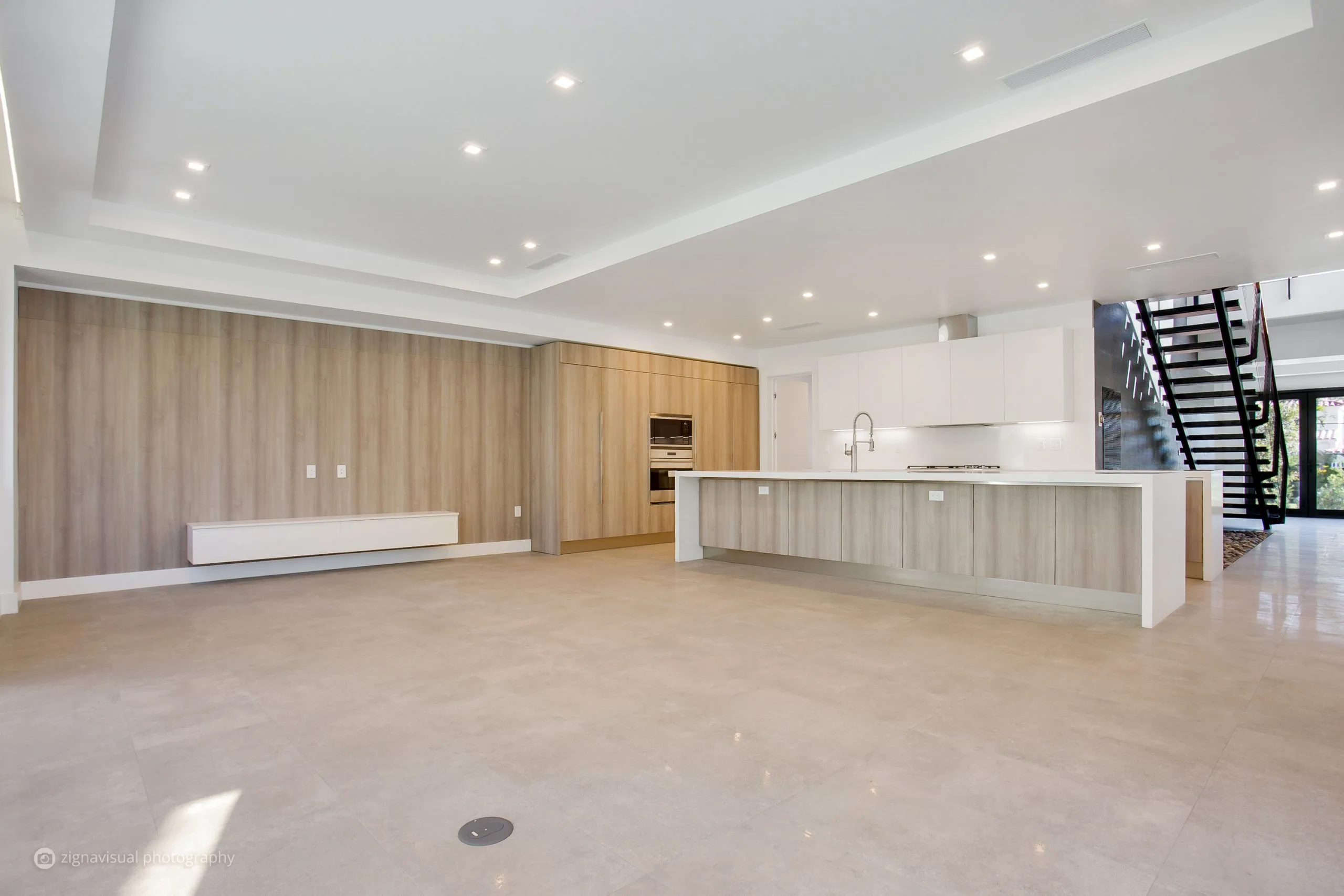 Open plan kitchen and living space with wood accent wall and black steel staircase in Miami Beach home