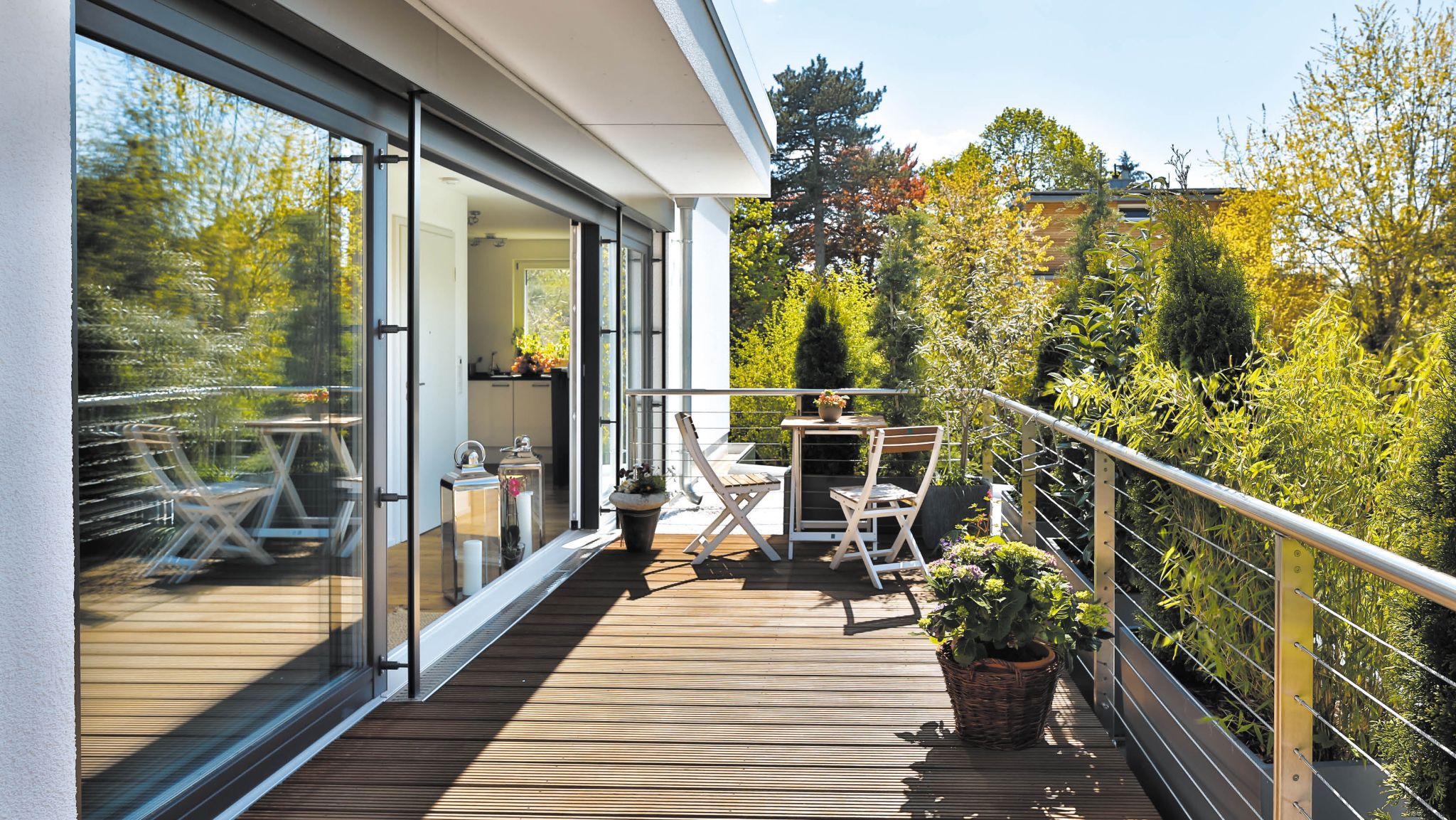 Moderne überdachte Holzterrasse mit Sitzgruppe, Glasfront und Blick auf üppige grüne Bäume.