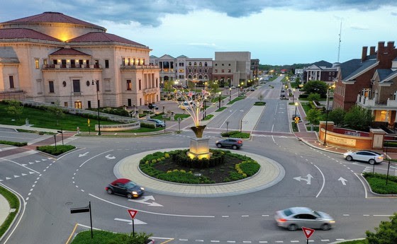 Aerial view of an intersecting dirt pathway forming an X-shape surrounded by lush greenery and arid, rocky terrain, illustrating a contrasting landscape.
