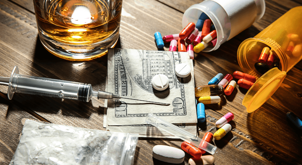 Image of lots of drugs, piills, open pill bottles, a syringe, a baggie with white powder in it, sitting on a table