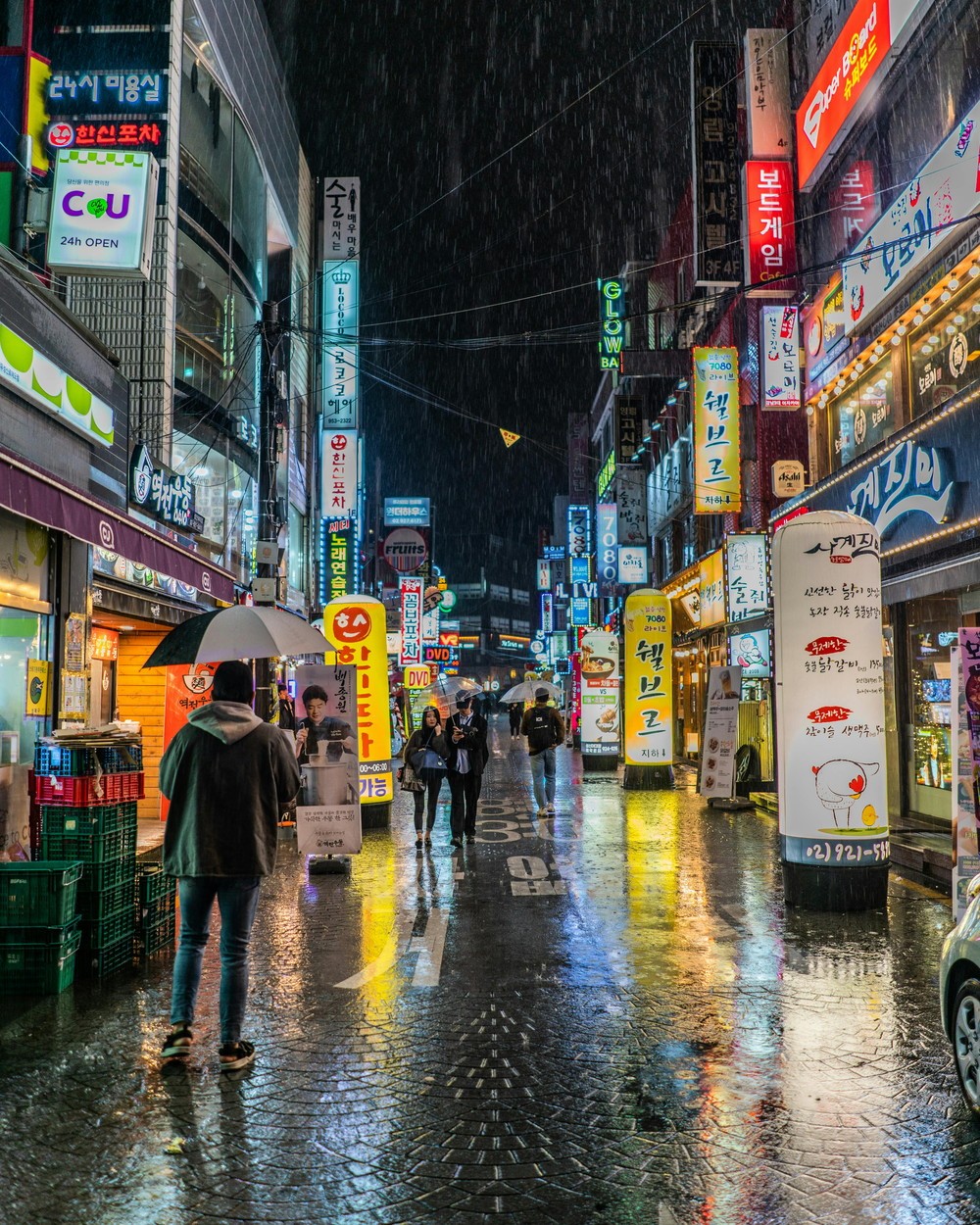 Neon-lit street in Seoul at night with pedestrians walking through the rain