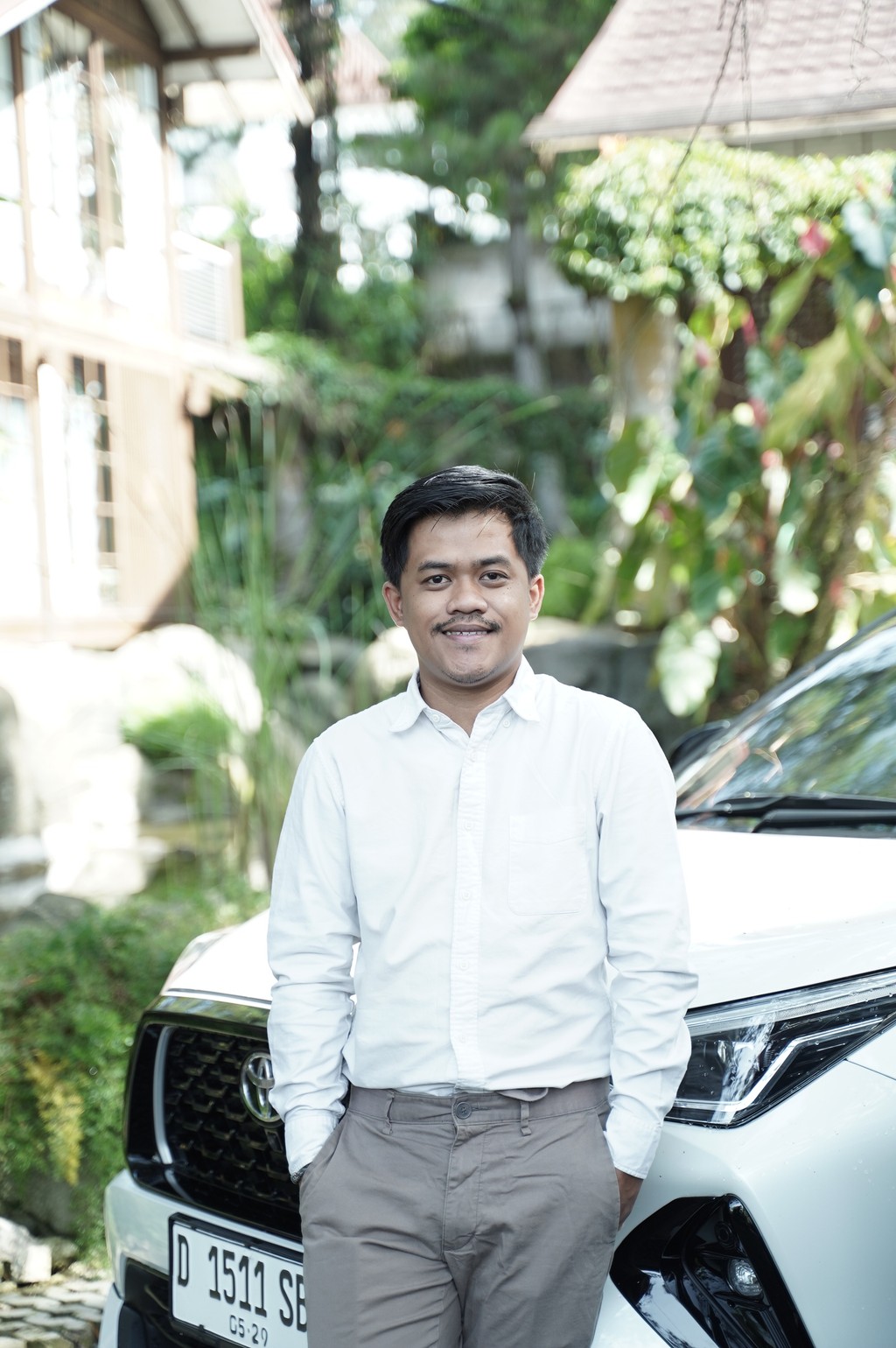 A winding road cuts through rocky terrain, surrounded by patches of green grass and illuminated by sunlight.