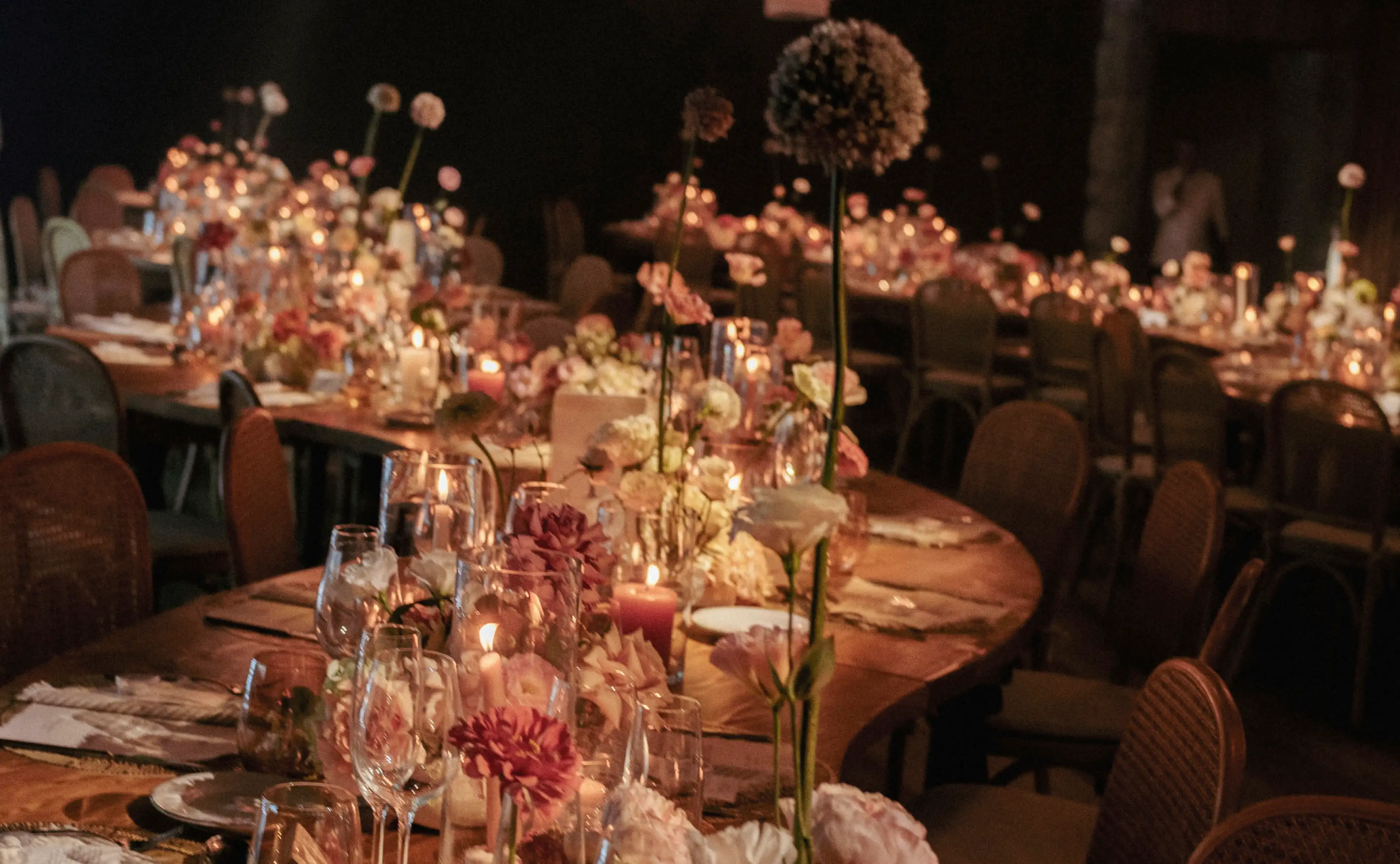 Ambiente nocturno con mesas iluminadas por velas y flores en tonos rosados, durazno y crema.