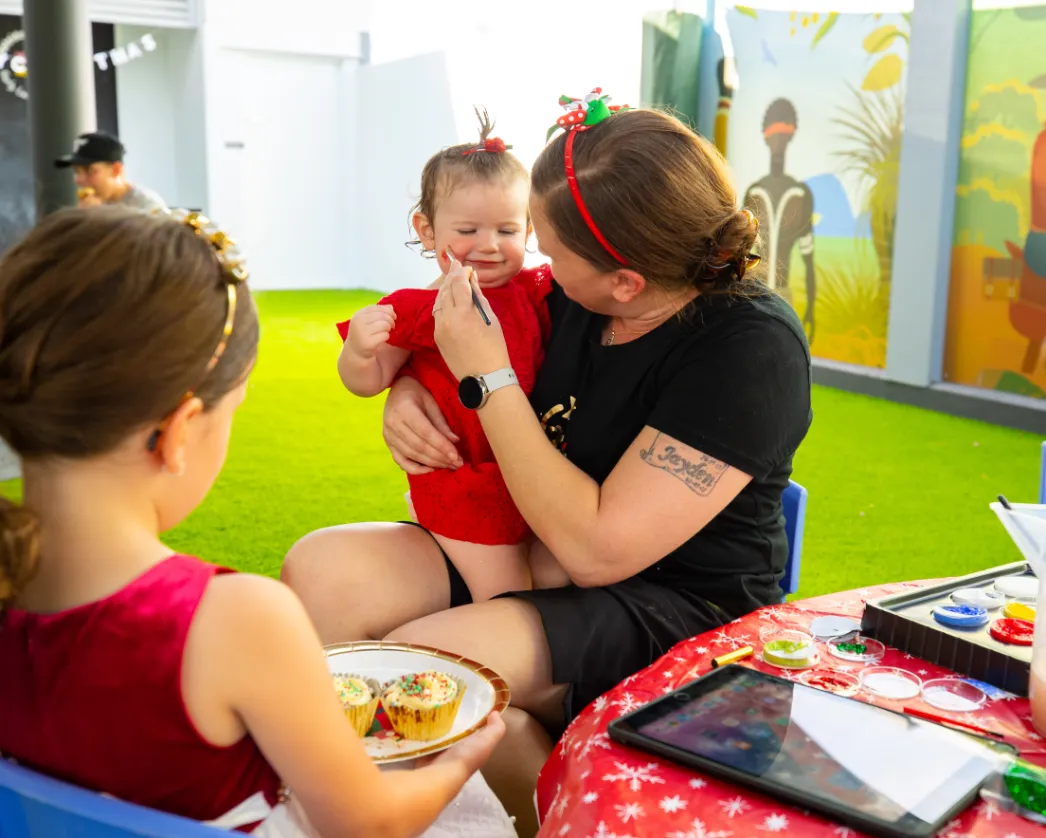 Educator comforting a toddler during craft and face painting at Kaleidoscope Kids childcare in Brisbane.