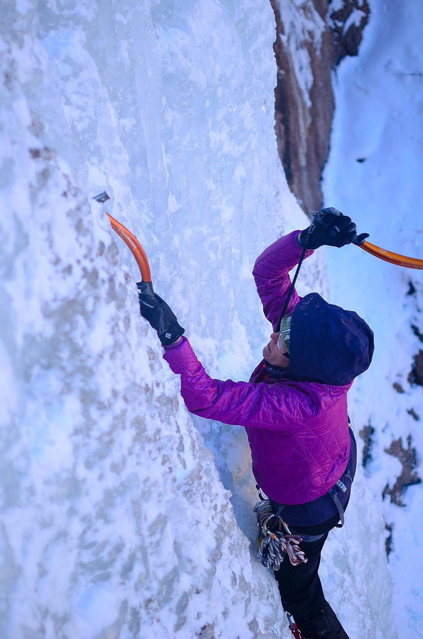 Ice climber leads above gear with ice tool ready to swing