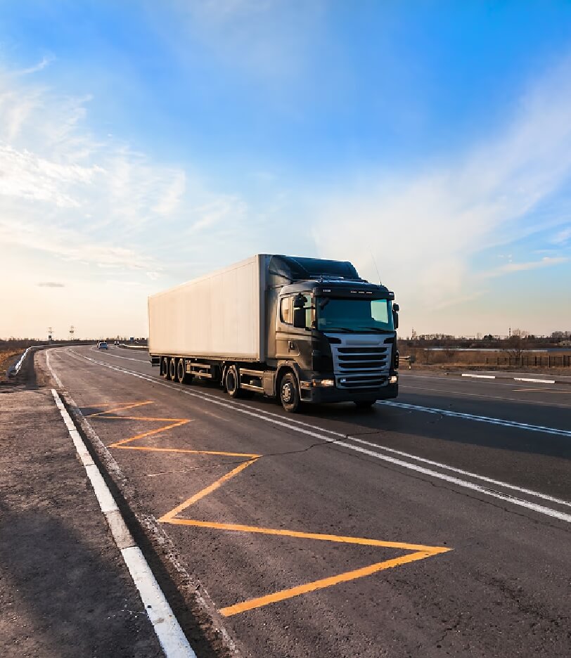 Large delivery truck on a highway under a clear blue sky, symbolizing logistics.