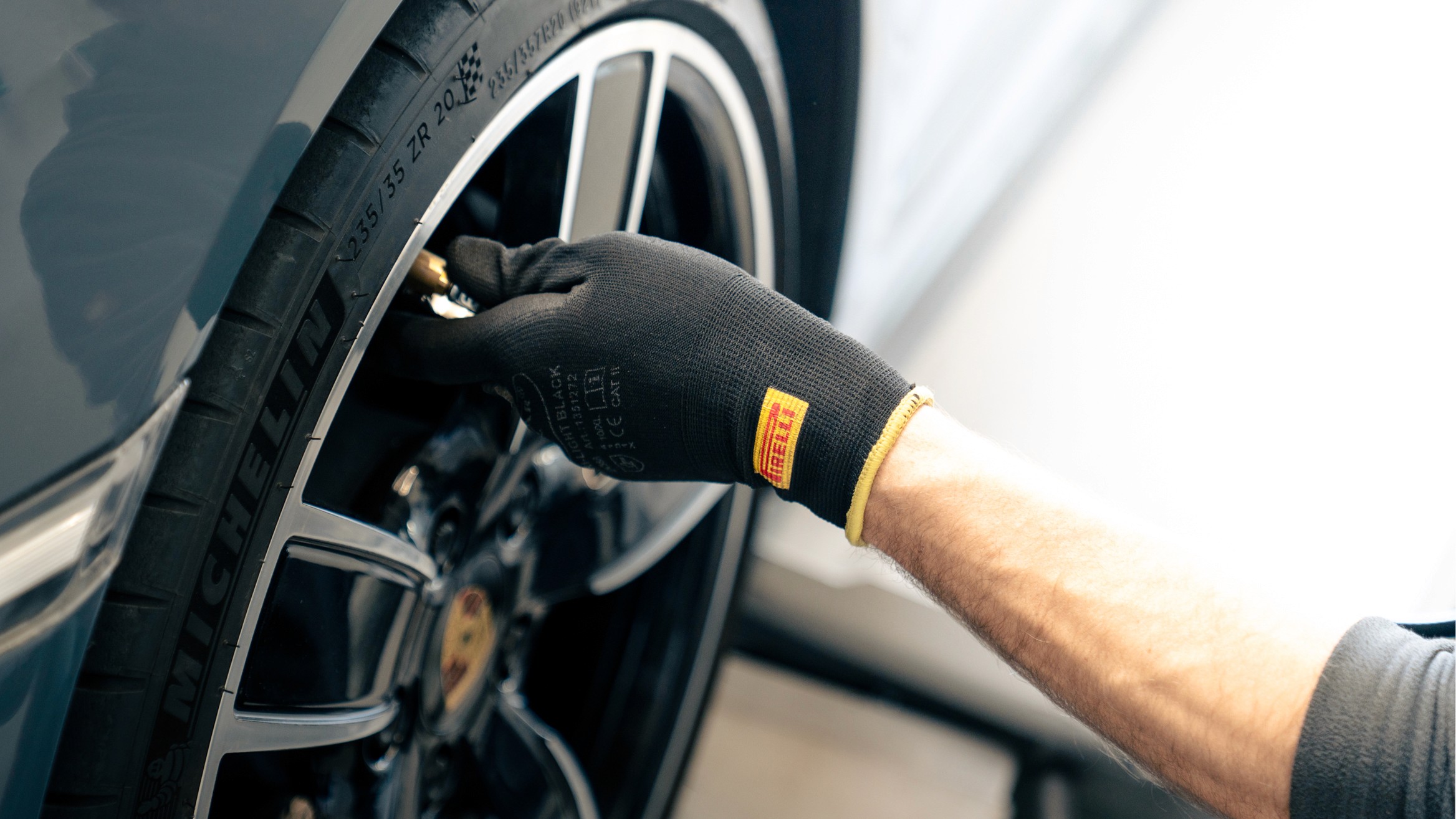 Mechaniker prüft den Reifendruck eines Porsche-Rades mit Handschuhen, Nahaufnahme von Felge und Ventil beim Service