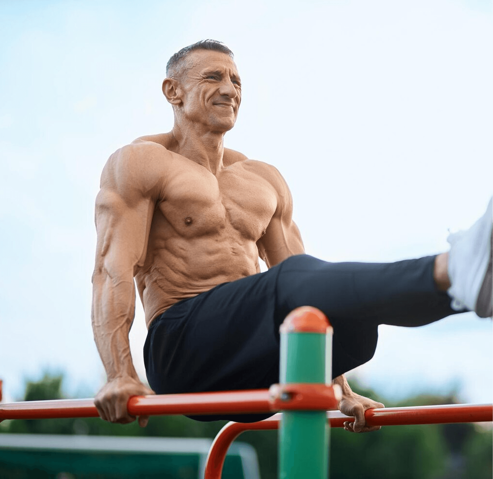 Shirtless muscular man doing an L-sit on outdoor parallel bars.