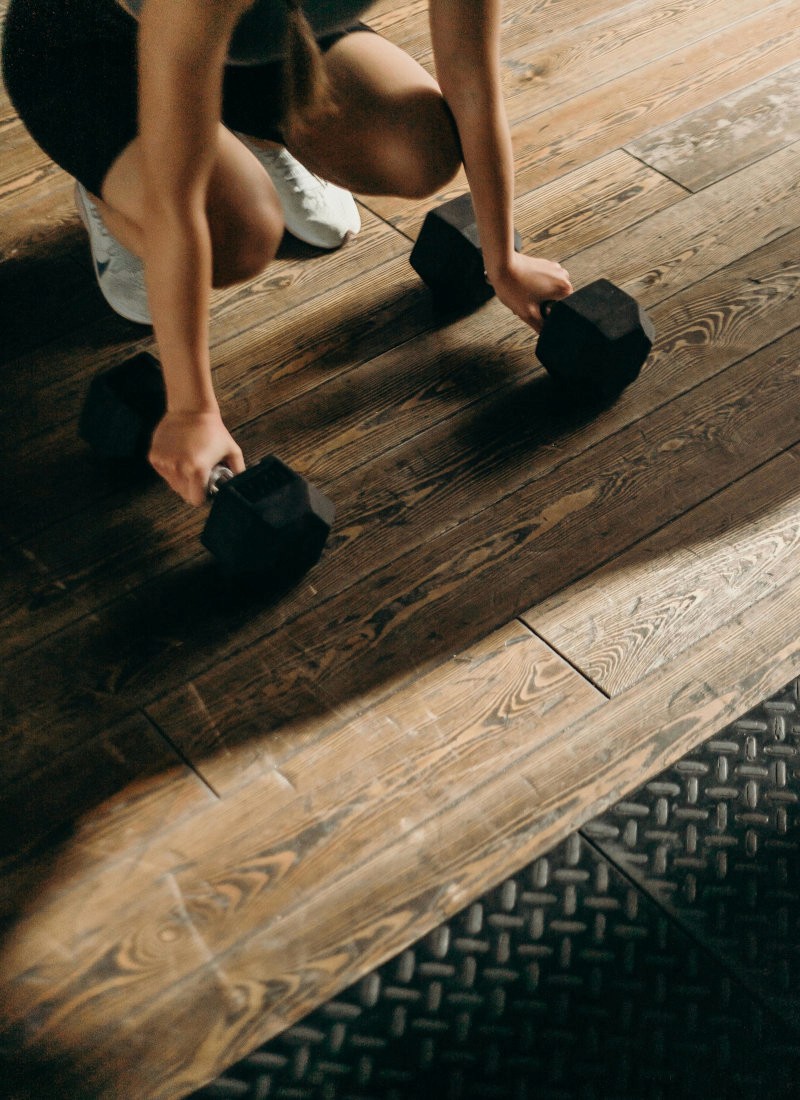 A woman crouching on a wooden floor holding dumbbells